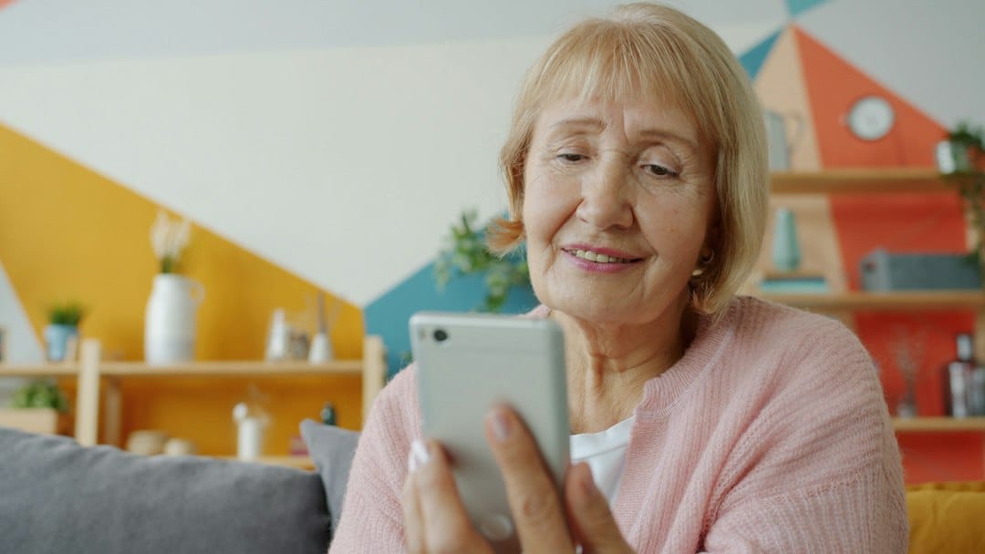 Personne âgée lisant un SMS sur son smartphone – arnaque au SMS paiement détecté